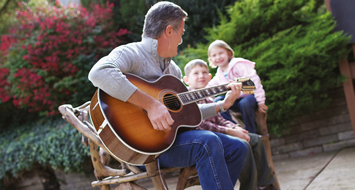 ein Mann, der mit einem Kind und einem M&auml;dchen Gitarre spielt