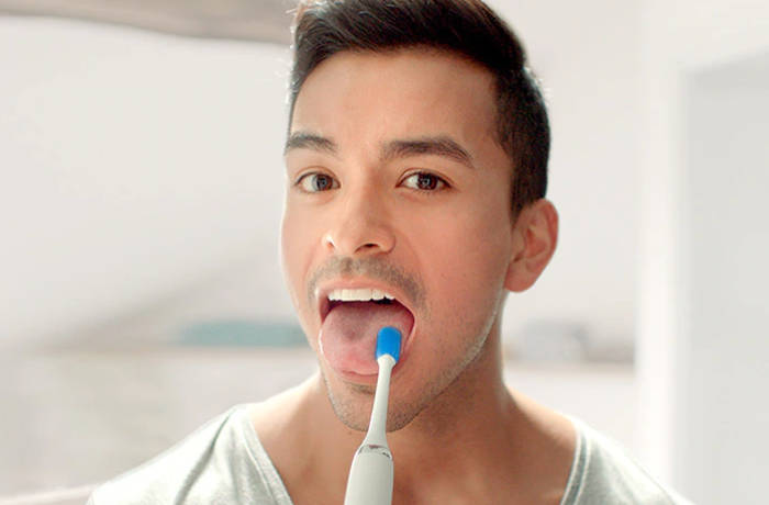 Ein Mann schaut in die Kamera und reinigt seinen Zungenbelag mit einer speziellen Philips Zungenb&uuml;rste.