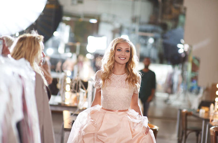 Eine Frau in einem hellrosa Kleid l&auml;chelt in die Kamera und zeigt dabei ihre wei&szlig;en Z&auml;hne.